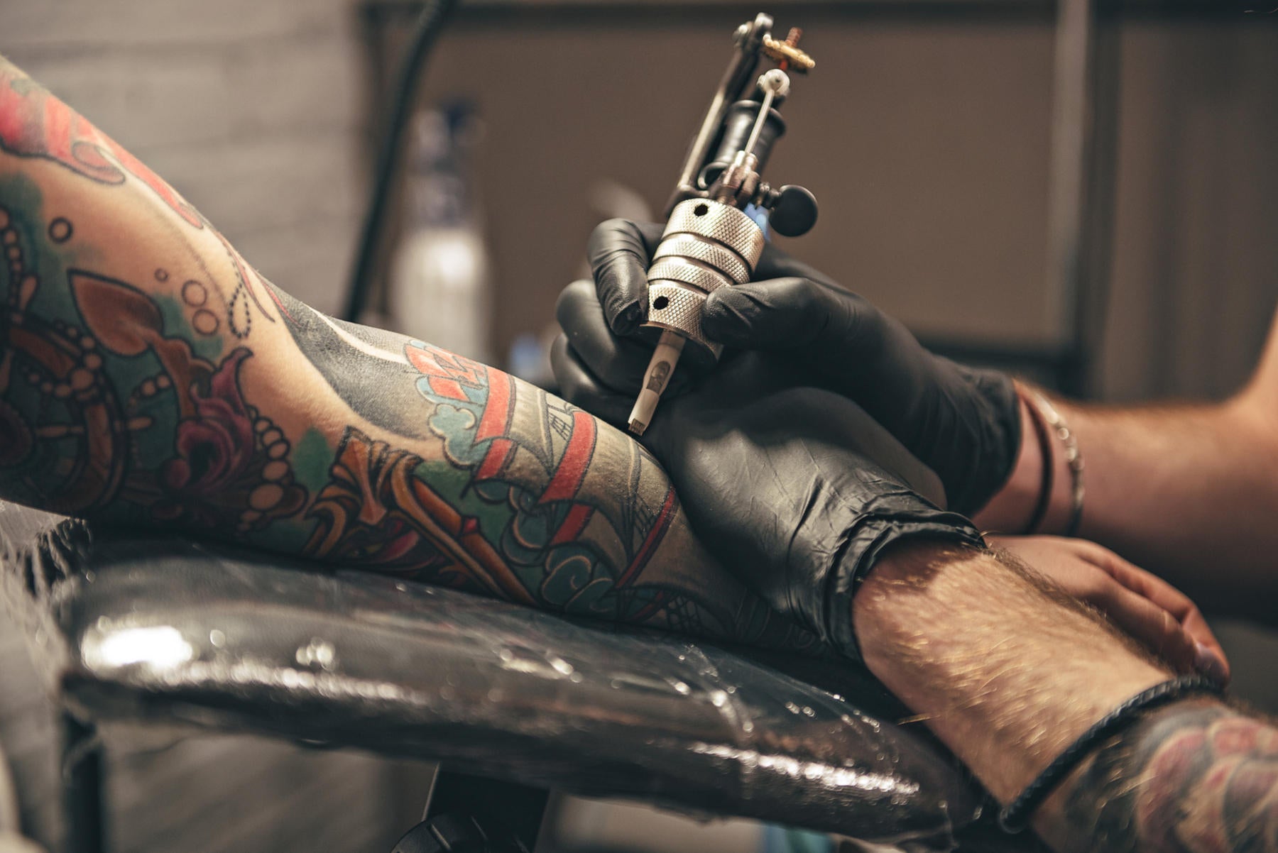 Tattoo artist tattooing a full color sleeve tattoo on persons arm