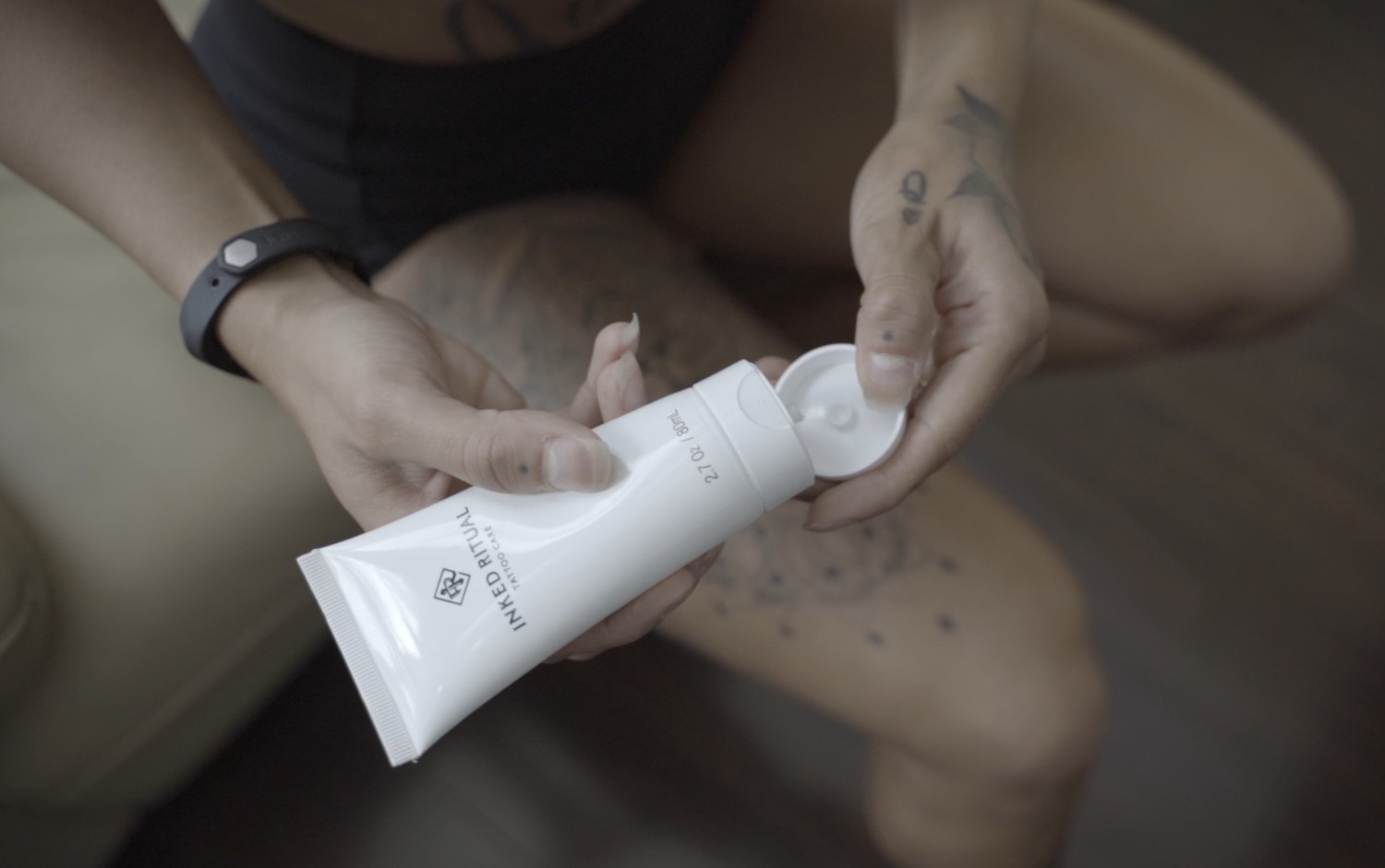 Individual opening a tube of Inked Ritual Tattoo Care cream, preparing to apply the formula on a tattooed leg, showcasing the product's ease of use.