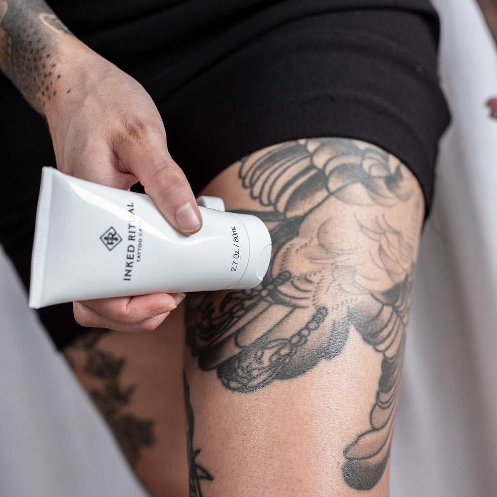 Hand applying Inked Ritual Tattoo Care lotion to a beautifully detailed thigh tattoo, showcasing the cream's use in maintaining ink clarity.