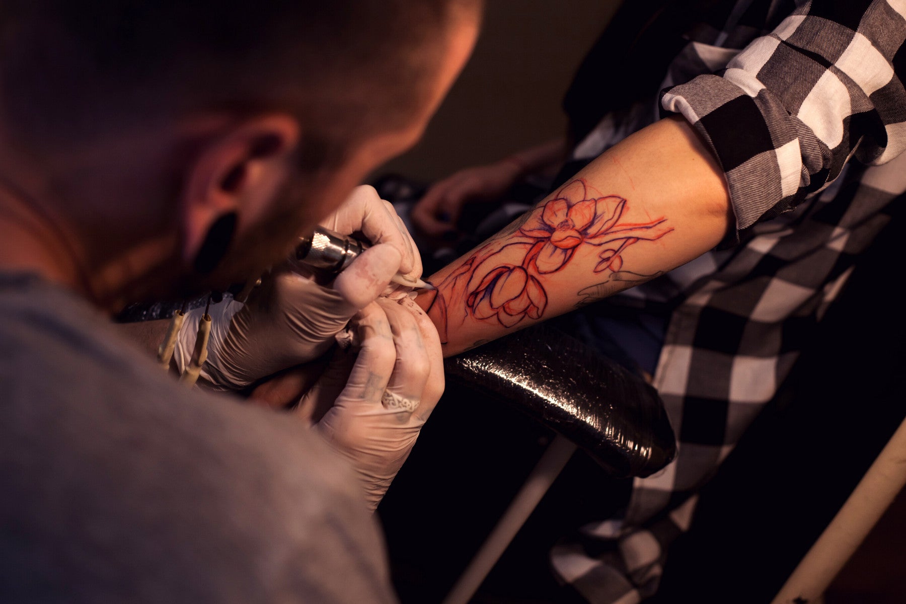 Male tattoo artist tattooing a large flower tattoo on a persons forearm