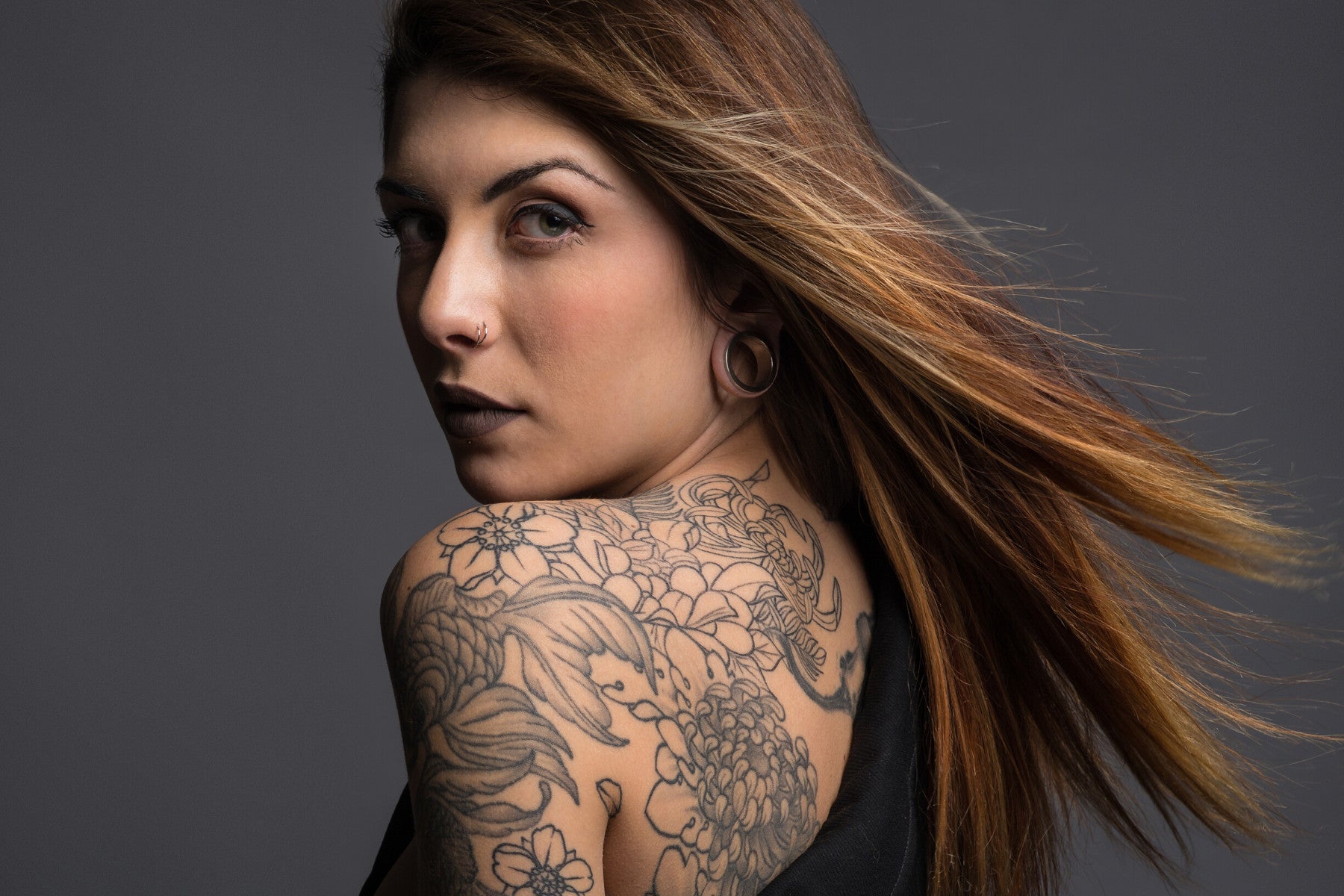 "Confident woman with a detailed floral shoulder tattoo looking over her shoulder, representing the effectiveness of Inked Ritual Tattoo Care in maintaining tattoo vibrancy compared to regular moisturizers and sunscreens.